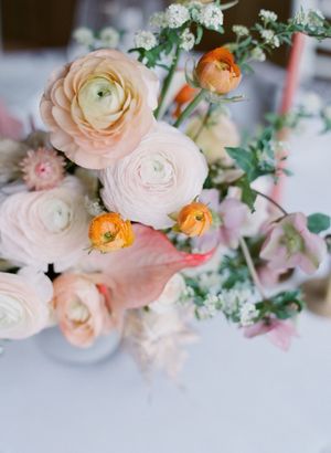 Lush wedding centerpiece featuring blush and orange ranunculus with white blooms and greenery on a white table.