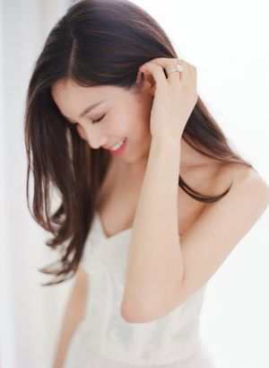 Smiling Asian bride in white dress touching hair with diamond engagement ring detail.