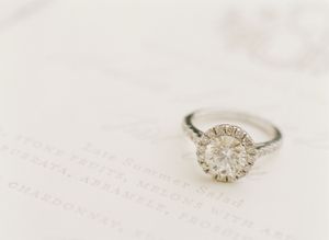 Elegant round halo diamond engagement ring resting on wedding menu card close-up.