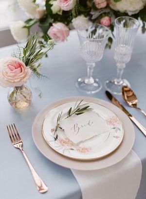 Elegant wedding place setting with gold cutlery, crystal glasses, and floral place card reading Bride.