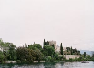 Scenic lakeside view of a grand castle surrounded by cypress trees and lush greenery.