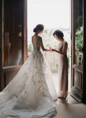 Bride in embroidered ball gown and mother share tender moment in doorway with scenic view.