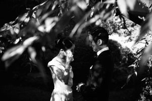 Black and white photo of bride and groom sharing an intimate moment under leafy trees.