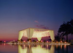 Stunning illuminated wedding pavilion with fairy lights reflecting over water at dusk.