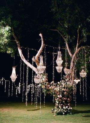 Enchanting outdoor wedding decor with crystal chandeliers and fairy lights hung from trees.