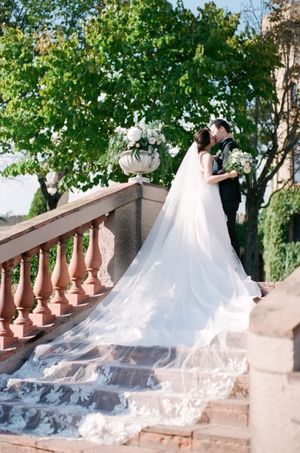 Bride and groom embracing on ornate stone staircase with a long lace cathedral veil.