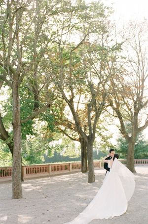 Bride and groom share romantic embrace under golden trees with flowing white wedding gown train spread wide.