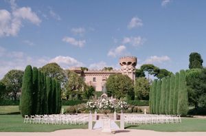 Outdoor wedding ceremony setup with white chairs on green lawn before a stunning historic castle venue.