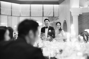Black and white photo of smiling bride and groom at sweetheart table during elegant wedding reception.