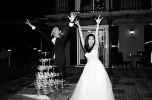 Joyful newlyweds celebrating with raised arms beside a champagne tower at their elegant wedding reception.