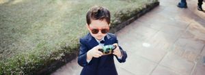 Adorable young boy in a suit and sunglasses photographing with a vintage camera at a wedding.