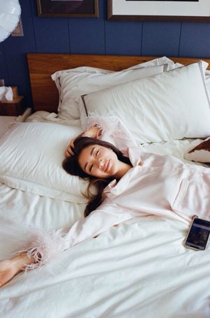 Happy woman in pink feather-trimmed pajamas smiling while relaxing in a cozy bed.