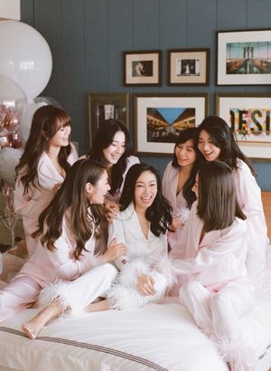 Bride surrounded by bridesmaids in matching pink pajamas sharing a joyful moment on a bed.