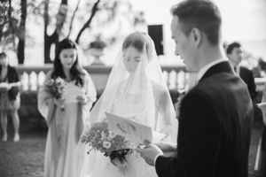 Bride in white gown and veil reading wedding vows during an elegant outdoor ceremony.