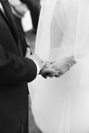 Close-up of bride and groom holding hands during their wedding ceremony in black and white.