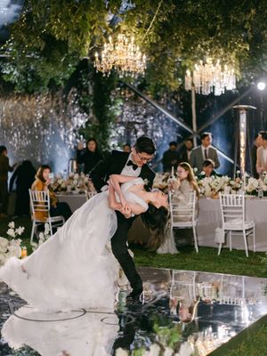 Groom dips bride on mirrored dance floor under crystal chandeliers at romantic garden wedding reception.