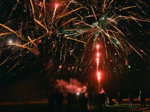 Colorful fireworks light up the night sky above silhouetted crowd at outdoor celebration.