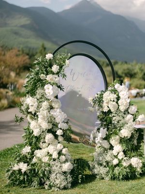 Circular floral arch with white blooms and greenery serves as elegant outdoor wedding welcome sign.