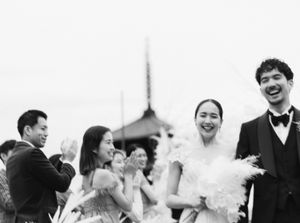 Joyful bride and groom laugh with guests during outdoor wedding ceremony in black and white photo.