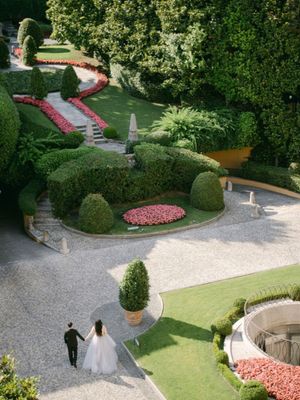 Aerial view of bride and groom strolling through an elegant Italian garden with manicured hedges.