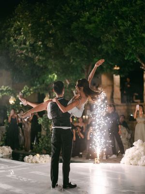Groom lifts bride dramatically on a sparkling dance floor with cold sparklers glowing nearby.