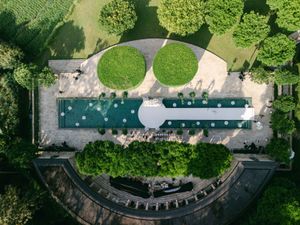 Aerial view of elegant wedding venue with lush green gardens, twin circular topiaries, and a rectangular reflecting pool.