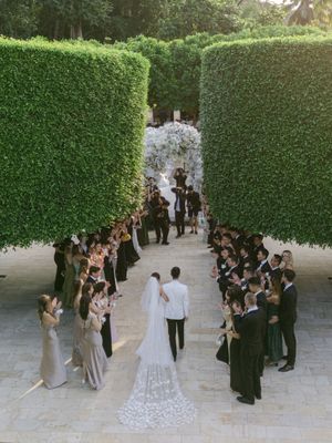 Wedding ceremony in a lush green hedge garden with bride and groom walking down the aisle surrounded by guests.