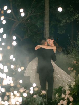 Bride and groom sharing a romantic first dance surrounded by glowing string lights and floral arrangements.