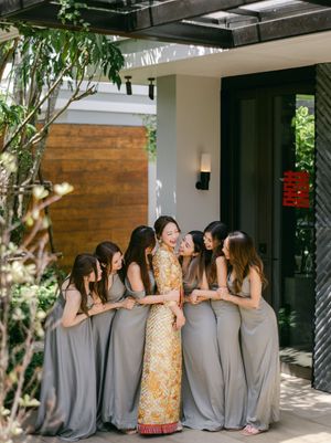 Bride in traditional Vietnamese ao dai gown surrounded by bridesmaids in grey dresses at a modern villa.