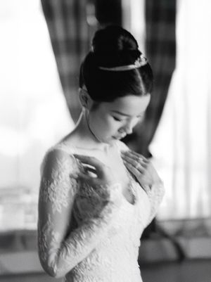 Black and white portrait of a bride in lace gown with elegant updo and tiara looking downward gracefully.