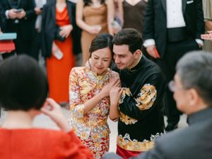 Couple in traditional Chinese wedding attire sharing tender moment during tea ceremony.