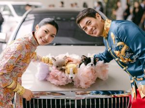 Smiling couple in Chinese wedding attire posing with stuffed animals on vintage car hood.