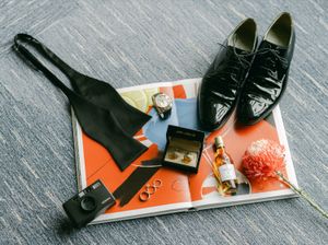 Groom wedding flat lay with black bow tie, dress shoes, cufflinks, rings, and cologne.