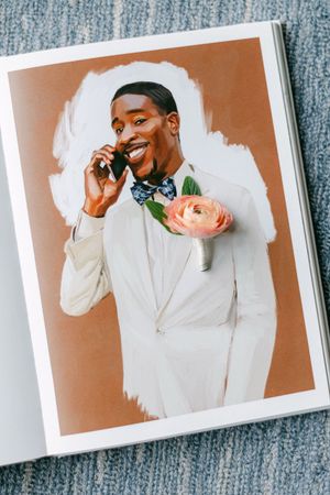Groom in white suit with floral boutonniere smiling while talking on phone, printed photo.