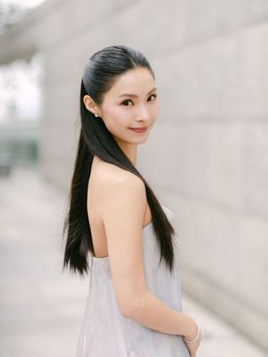 Elegant Asian bride with long straight hair in strapless gown posing against stone wall.
