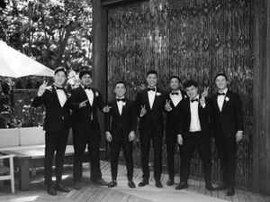 Groom and groomsmen in black tuxedos pose playfully in black and white photo.