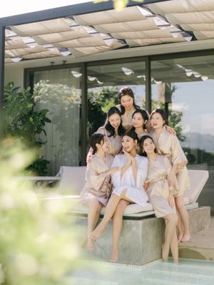 Bride and bridesmaids in robes laugh together poolside at a luxury villa.