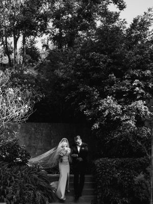 Bride and groom walk together in lush garden setting in a dramatic black and white photo.