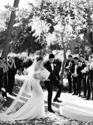 Bride and groom celebrate at outdoor ceremony as guests cheer in black and white photo.