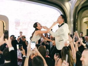 Joyful bride and groom celebrate on dance floor surrounded by cheering guests at wedding reception.