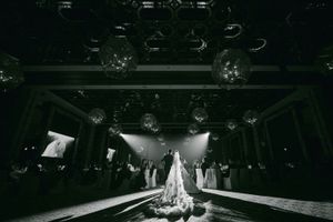 Black and white dramatic shot of bride standing alone on dance floor with disco balls overhead.