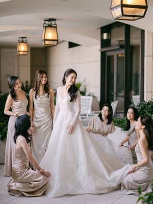 Radiant bride in a long-sleeve lace ball gown surrounded by smiling bridesmaids in champagne satin dresses on an elegant terrace.