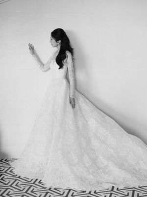 Black and white portrait of a bride in a long-sleeve lace ball gown with an dramatic train on a geometric tile floor.