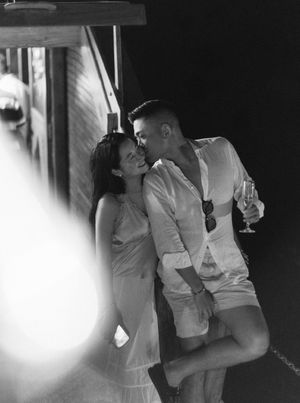 Romantic black and white photo of a couple sharing an intimate kiss outdoors at night, man holding a champagne glass.
