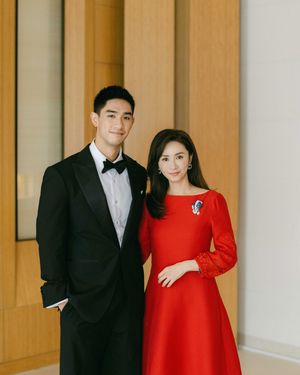 A couple poses elegantly, man in black tuxedo and woman in red dress, at a formal event.