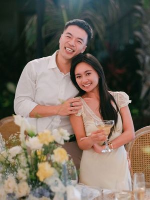 A smiling couple poses together at an outdoor garden engagement party with floral centerpieces.