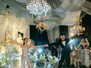 A bride and groom share their first dance under crystal chandeliers in a glamorous ballroom.