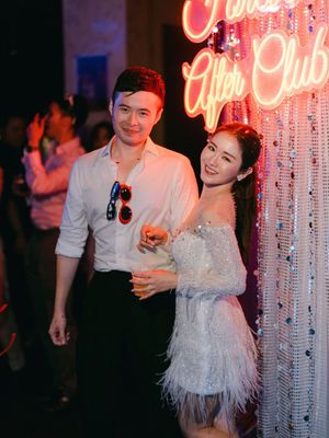 A couple smiles together in front of a neon After Club sign at a wedding after-party.