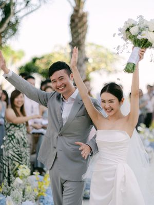 A joyful bride and groom celebrate with raised arms after their outdoor wedding ceremony.