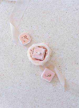 Diamond engagement ring displayed in blush pink velvet ring box with monogrammed lid and satin ribbon.